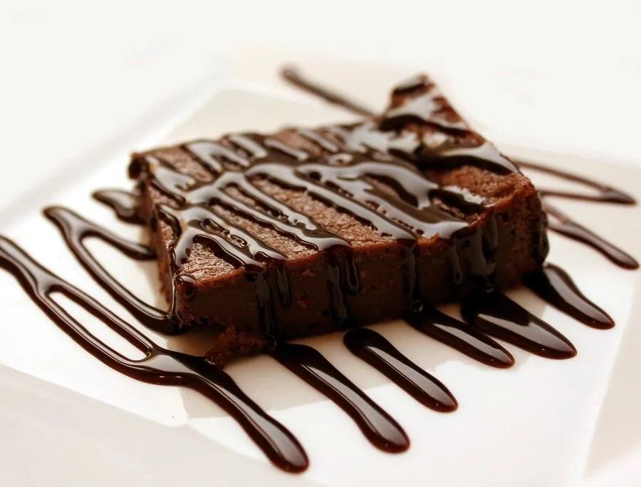 Potongan brownies cokelat dengan hiasan saus cokelat di piring putih