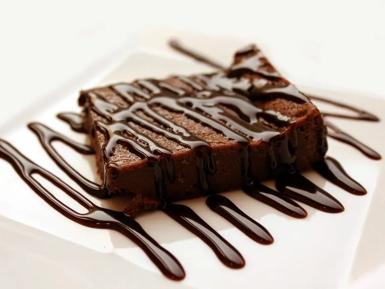 Potongan brownies cokelat dengan hiasan saus cokelat di piring putih