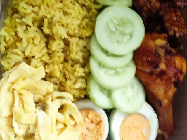 Nasi kuning dalam box dengan telur, timun, dan ayam goreng