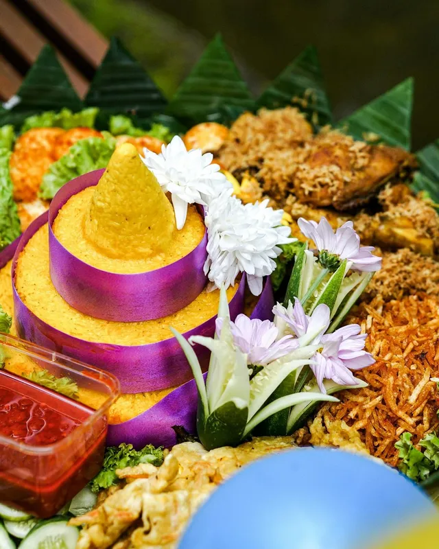 Tumpeng nasi kuning dengan hiasan sayur dan lauk di sekelilingnya