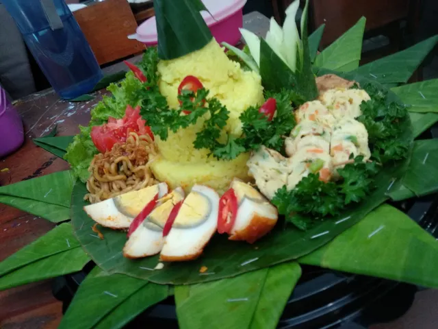 Tumpeng nasi kuning dengan telur dan lauk di atas daun pisang